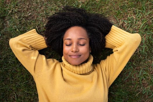 Young African American woman rest lying on grass with eyes closed. Lifestyle and relaxation concept.