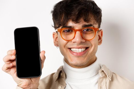 Face of handsome smiling guy in glasses showing empty smartphone scree, white background.