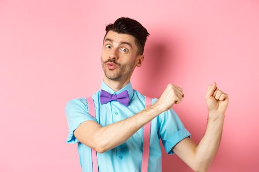 Image of funny guy dancing and celebrating holiday, enjoying party, standing over pink background.