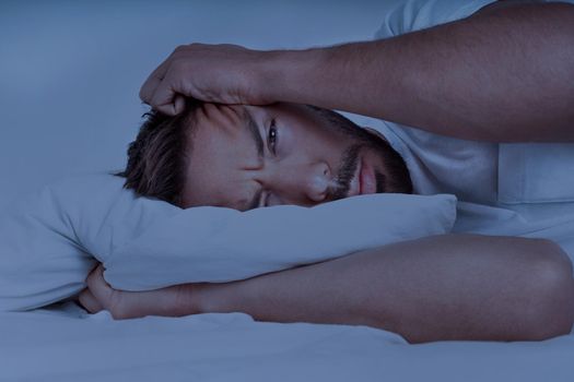 Young man lying in the bed and trying to sleep, can't sleep. Man suffering from insomnia, sleeping problems or sleep disorders. High quality photo