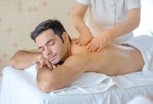 Handsome man enjoy with Thai masseuse massage to him and he lie on bed in spa room with day light.