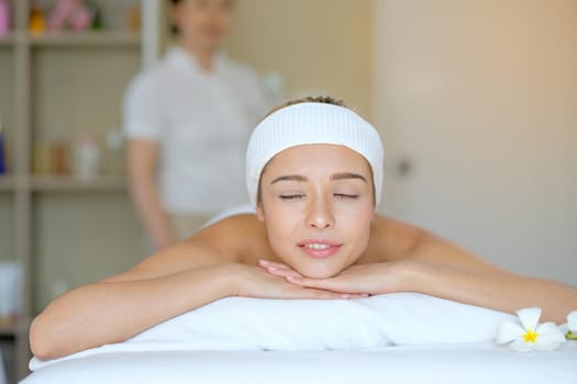 Portrait of White beautiful woman lie on bed in spa room and look relax and happy with Thai masseuse stand behind as background.