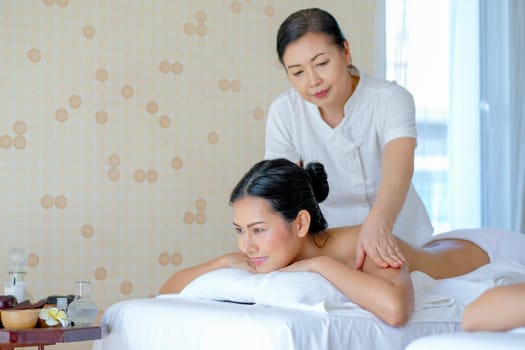 Thai masseuse massage for young Asian beautiful girl who lie on bed in spa room with day light.