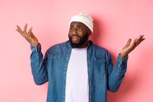 Skeptical confused man looking at something riddiculous, staring left and shrugging, raising hands up puzzled, standing over pink background.