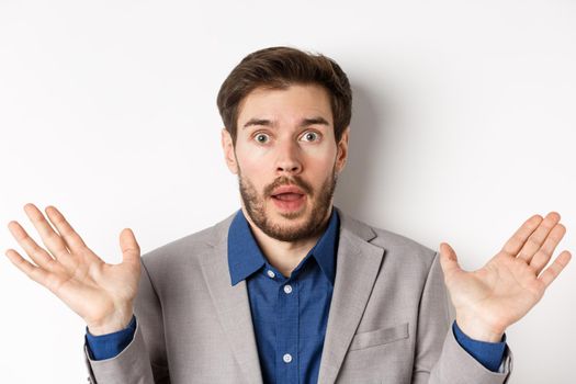 Surprised business man in suit spread hands sideways, looking confused and startled, white background.