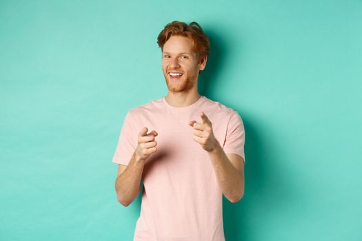 Funny redhead guy congratulating you, pointing fingers at camera and smiling, making choice, standing in t-shirt over mint background.