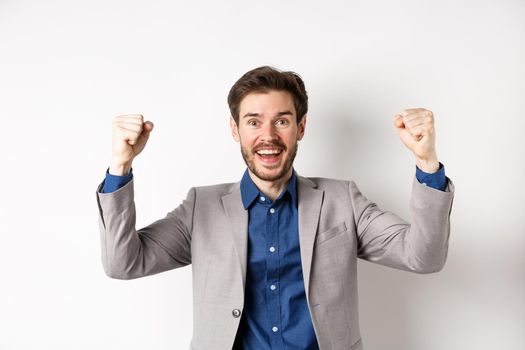 Happy man in suit raising hands up and chanting, watching sports game, winning in casino and celebrating, standing excited on white background.