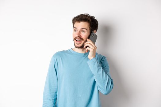 Technology concept. Cheerful man talking on mobile phone, having phone call and looking amused, standing over white background.