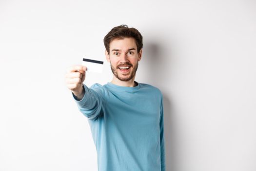 Happy man showing plastic credit card and smiling, recommending bank, standing over white background.