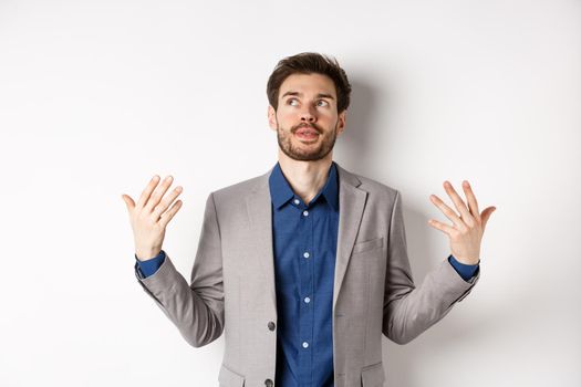 Tensed young manager in suit need some air, waving at himself as feeling flushed and annoyed, standing on white background.