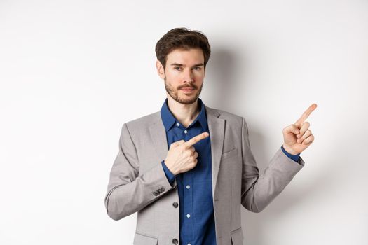 Confident handsome man in business suit pointing at upper right corner logo, showing company banner and smiling assertive, standing on white background.