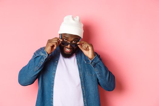 Confused african-american guy stare at camera, take-off sunglasses an looking puzzled, standing over pink background.