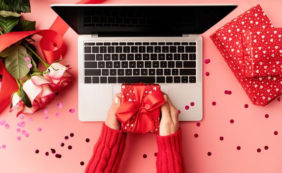Valentines Day concept. Female hands holding a red valentine gift box top view on pink background. Top view of pink desktop with flowers and gift boxes
