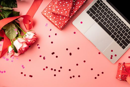 Valentines Day concept. Top view of valentines day workspace with laptop keyboard, confetti, flowers and gift boxes
