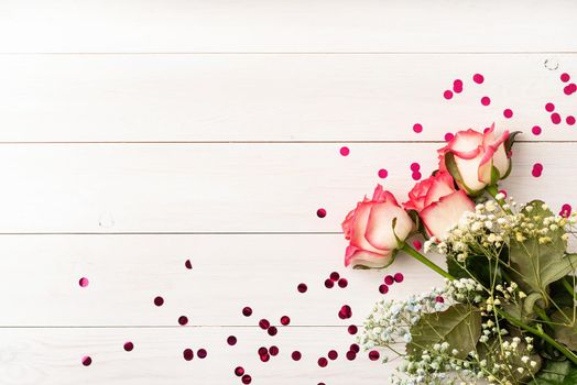 Valentines Day concept. Pink roses with confetti on white wooden background