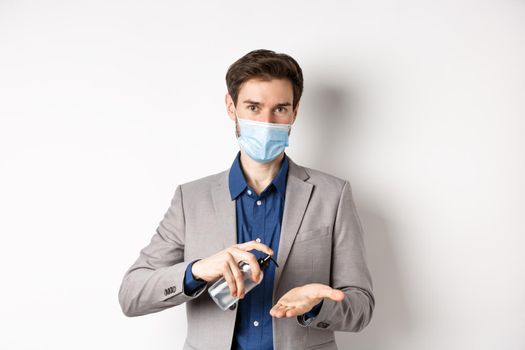 Covid-19, pandemic and business concept. Male office worker clean hands with antiseptic, using sanitizer and looking at camera, wearing medical mask.