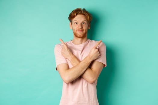 Attractive indecisive man in t-shirt cross hands and pointing sideways, showing two choices, need help with decision, standing over turquoise background.