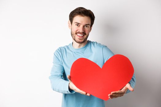 Happy gay man giving big red heart to his lover on valentines day, concept of romantic date and love celebration, standing over white background.