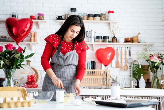 Valentines Day. Woman in red dress and gray apron making valentine cookies at the kitchen