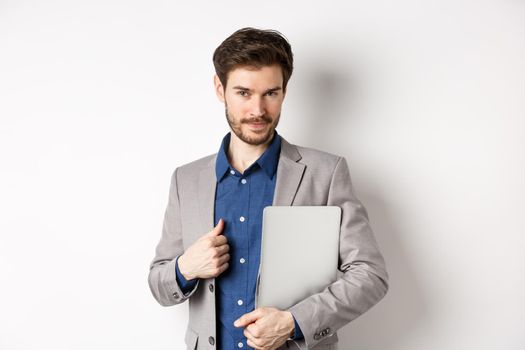 Successful businessman in stylish suit carry laptop and looking confident at camera, smiling pleased, white background.