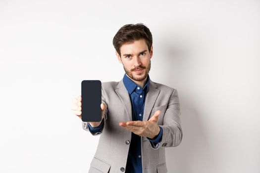 E-commerce and online shopping concept. Man demonstrated empty smartphone screen to you, showing phone display to introduce something, standing on white background.