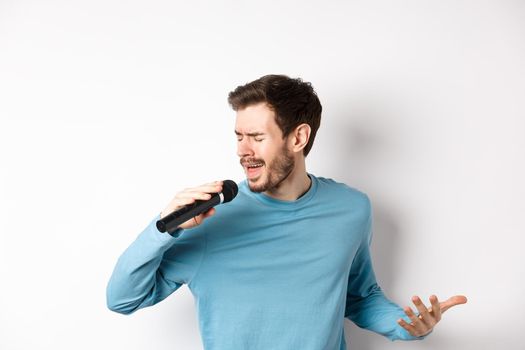 Singer performing song on white background. Young man singing in microphone at karaoke.