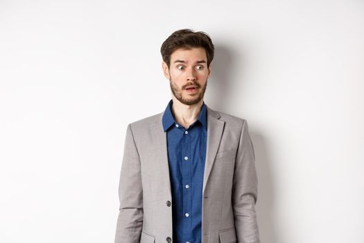 Shocked male entrepreneur in suit looking aside at logo with startled face, standing on white background.