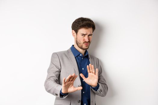 Stay away. Reluctant businessman step back with concerned disgusted face, raising hands to block bad offer, rejecting something awful, telling no and decline proposal, white background.