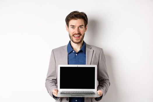 Handsome caucasian businessman in suit showing empty laptop screen, demonstrate promo, standing on white background.