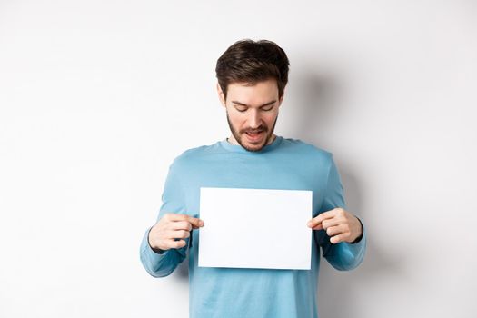 Excited bearded guy reading banner on blank piece of paper, showing logo, standing over white background.