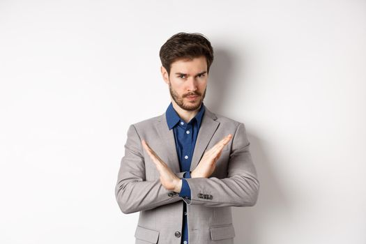 Serious business man making cross and says no, looking determined, disagree and prohibit something bad, tell to stop, standing in suit on white background.