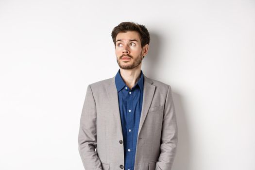 Thoughtful sad businessman in suit looking at upper left corner logo, thinking or spacing out, standing on white background.