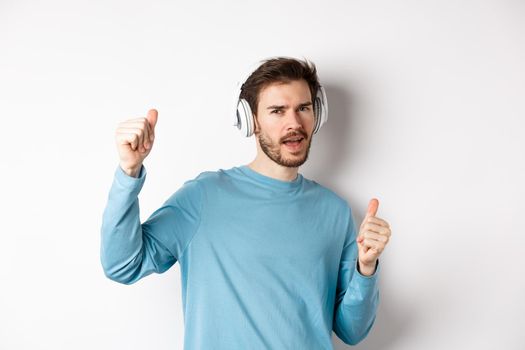 Cheeky guy dancing and having fun in wireless headphones, enjoying good sound quality, white background.