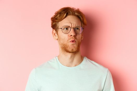 Ouch thats bad. Face of redhead man showing pity and feeling sorry for someone, frowning and looking with compassion, standing over pink background.