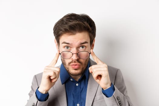 Surprised businessman takes-off glasses and look excited at camera, checking out interesting deal, standing on white background.