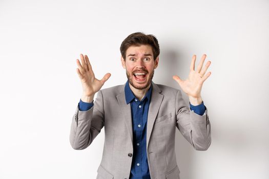 Businessman scream and shake hands in panic, look alarmed and anxious, shouting at camera, standing in suit on white background.