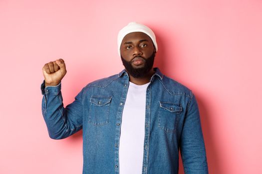 Serious and confident african-american male activist, raising fist, support Black lives matter BLM movement, fight for human rights against racism, pink background.