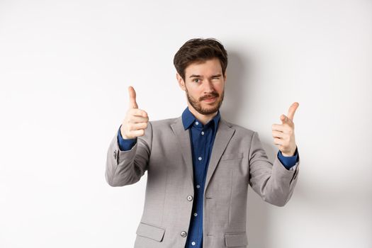 You got this. Handsome caucasian businessman in suit pointing fingers at camera and winking, motivating people, inviting to work in company, standing on white background.