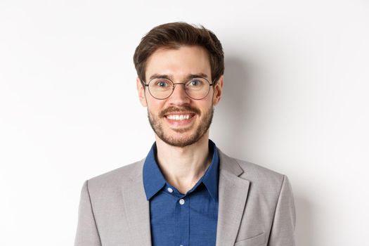 Close-up of handsome young office worker in glasses and suit smiling at camera, looking happy on white background.