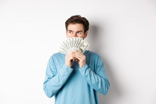 Dreamy man thinking of buying product, holding money and looking left pensive, imaging shopping, standing over white background.