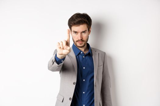 Listen to me. Serious male ceo manager showing one finger, scolding or telling to stop, tell no, hold right there sign, standing on white background in suit.