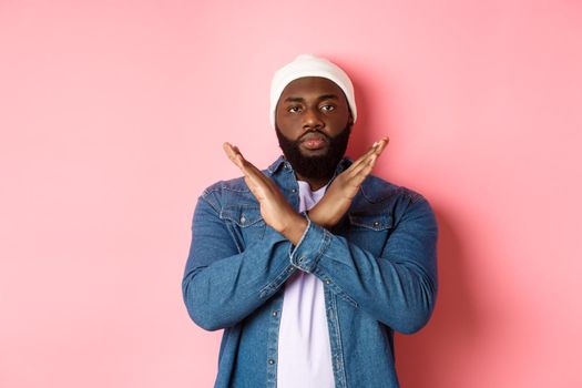 Serious african-american man saying no, showing cross to stop something bad, prohibit action, standing over pink background.