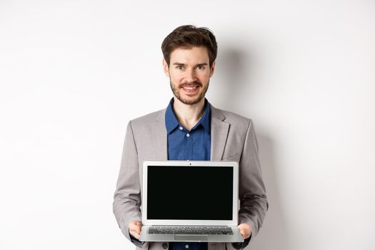 Handsome caucasian businessman in suit showing empty laptop screen, demonstrate promo, standing on white background.