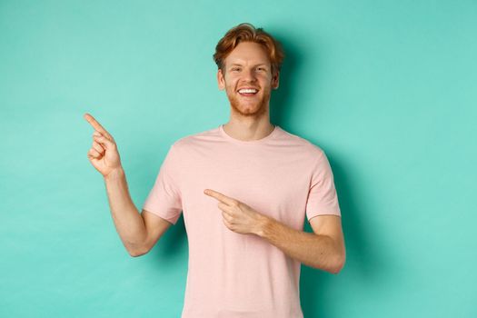 Attractive caucasian man in t-shirt pointing fingers left, smiling happy and showing advertisement, standing over turquoise background. Copy space