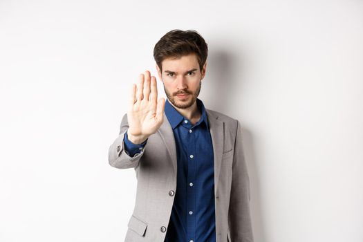 Hold right there. Serious businessman in suit stretch out hand and tell to stop, frowning and look confident, disapprove action, prohibit something bad, standing on white background.