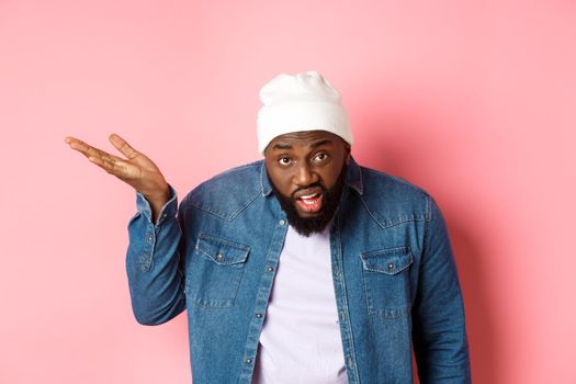 Annoyed and pissed-off Black man arguing, staring at camera and scolding person, standing over pink background.