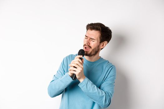Romantic man singing song in microphone at karaoke, standing over white background.