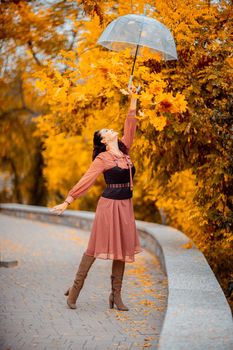 Beautiful girl in a dress with an umbrella in the autumn park. She holds him over her head, autumn leaves are falling out of him.