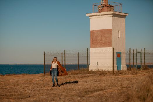 A woman walking along the coast near the sea. An elegant lady in a brown coat and a hat with fashionable makeup walks on the seashore.