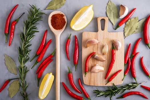 Pods of red hot pepper among other spices on gray surface with plaster texture. Healthy and wholesome food, food preparation. Selective focus. View from above.